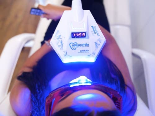 A woman sits back to relax while the laser light teeth whitening gel gets to work. Image taken above showing the laser light emitting blue light onto the lady's mouth
