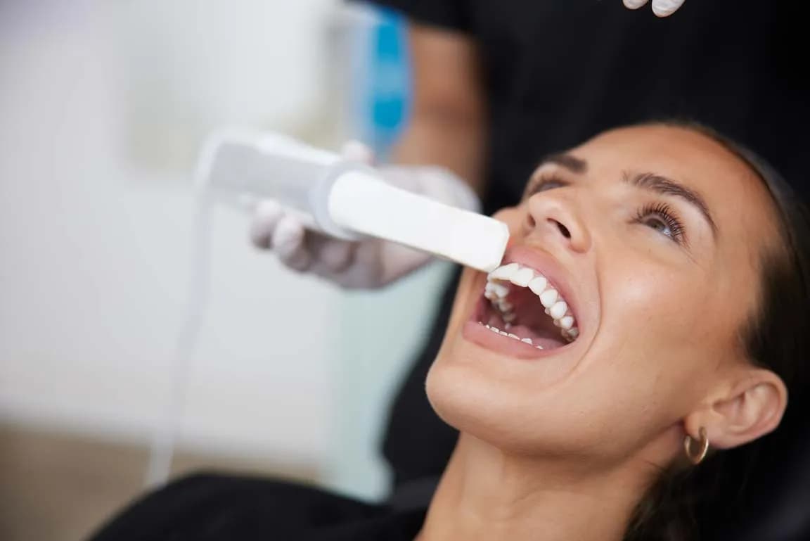 Dentist using an intraoral scanner on a woman's open mouth during a dental examination.