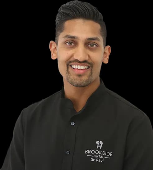 Smiling man wearing a black dental uniform with Brookside Dental logo and name Dr Ravi.