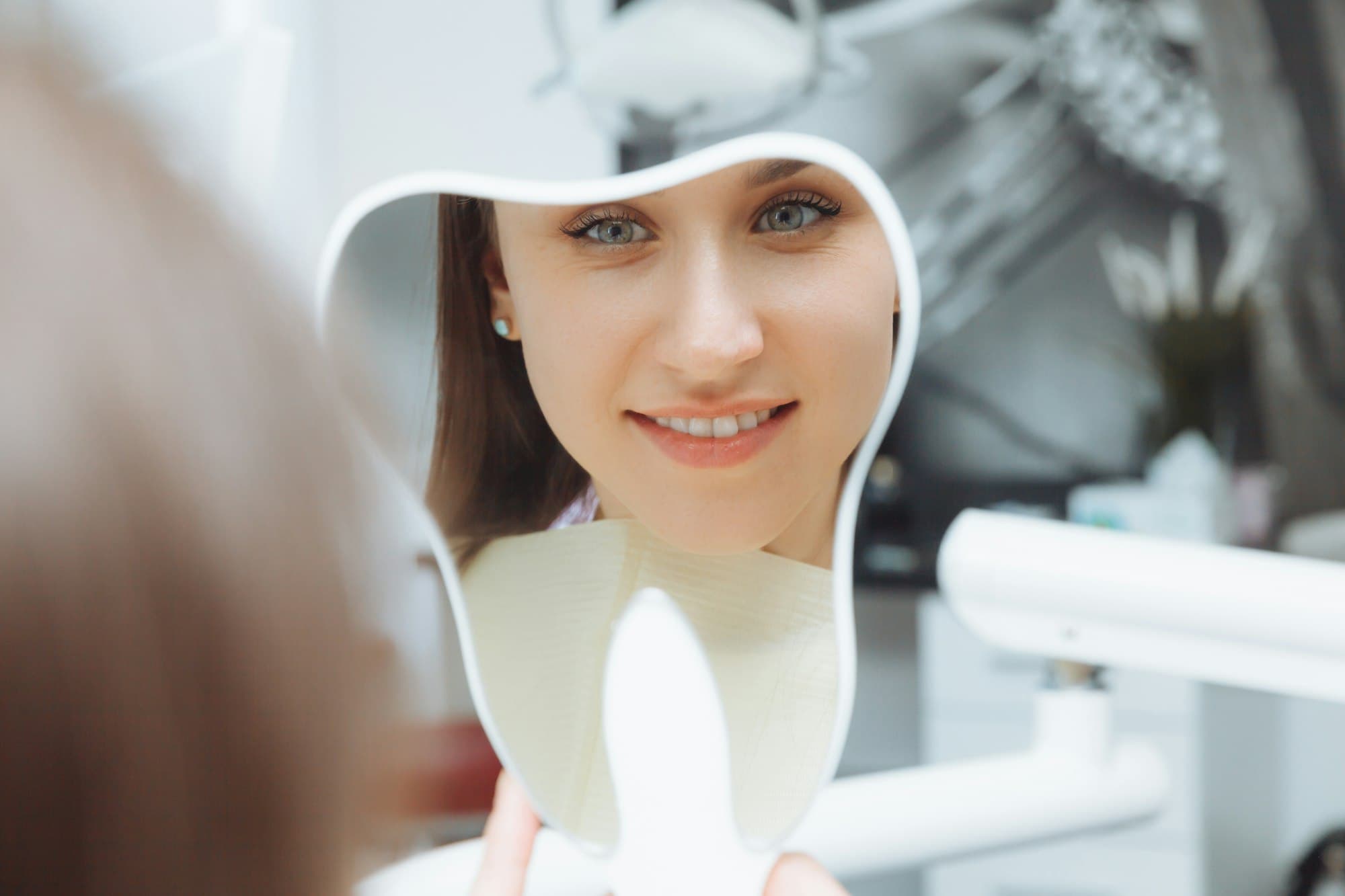 A young woman patient looks at her teeth in the mirror. Modern dental clinic. teeth whitening