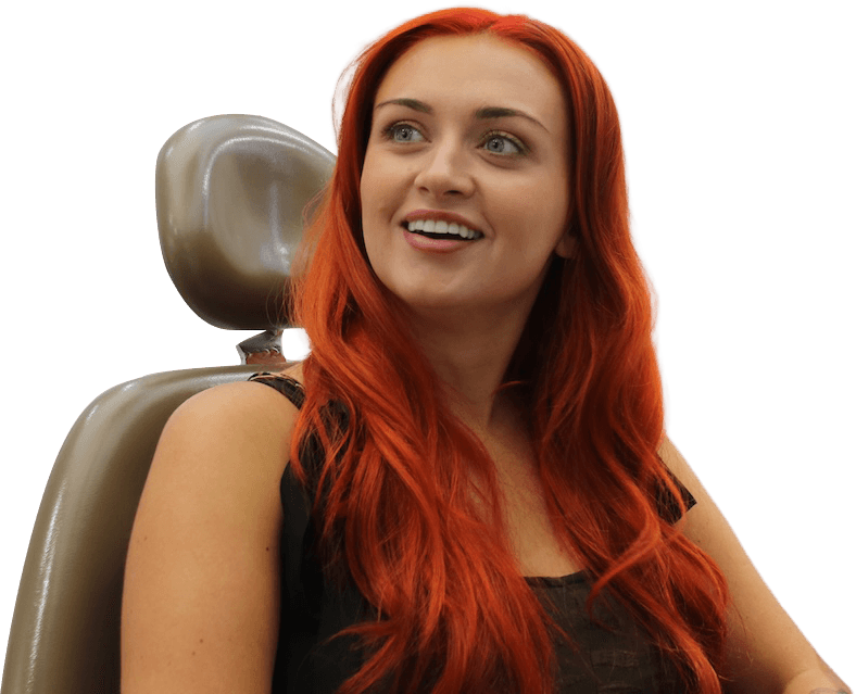 Smiling woman with long red hair sitting on a brown chair and looking to the side.