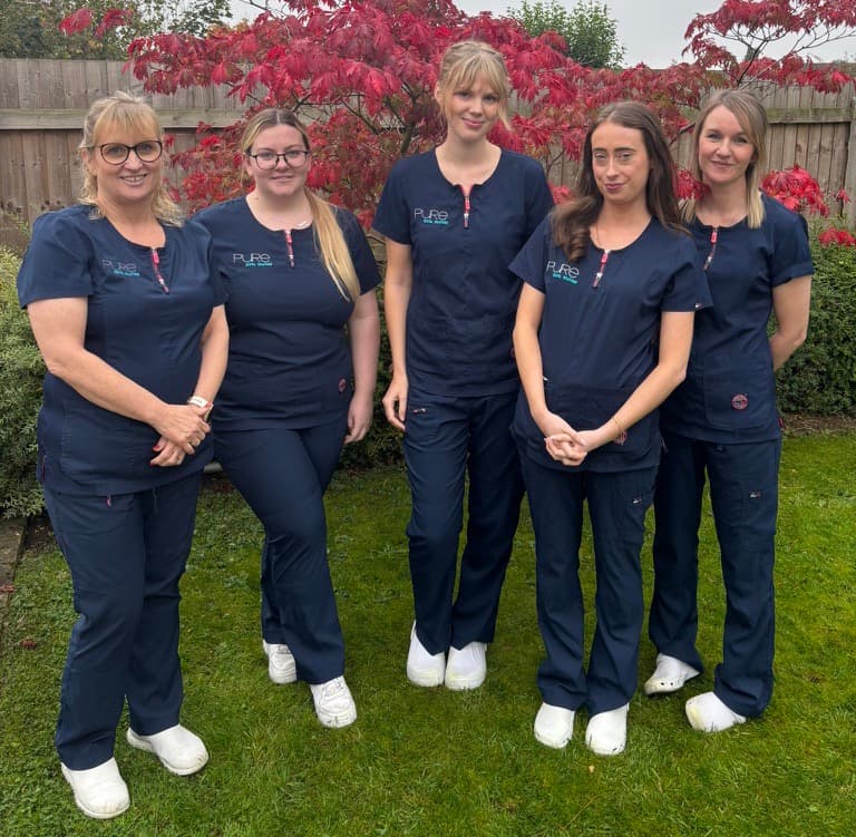 Dental team posing for a picture with a green background.