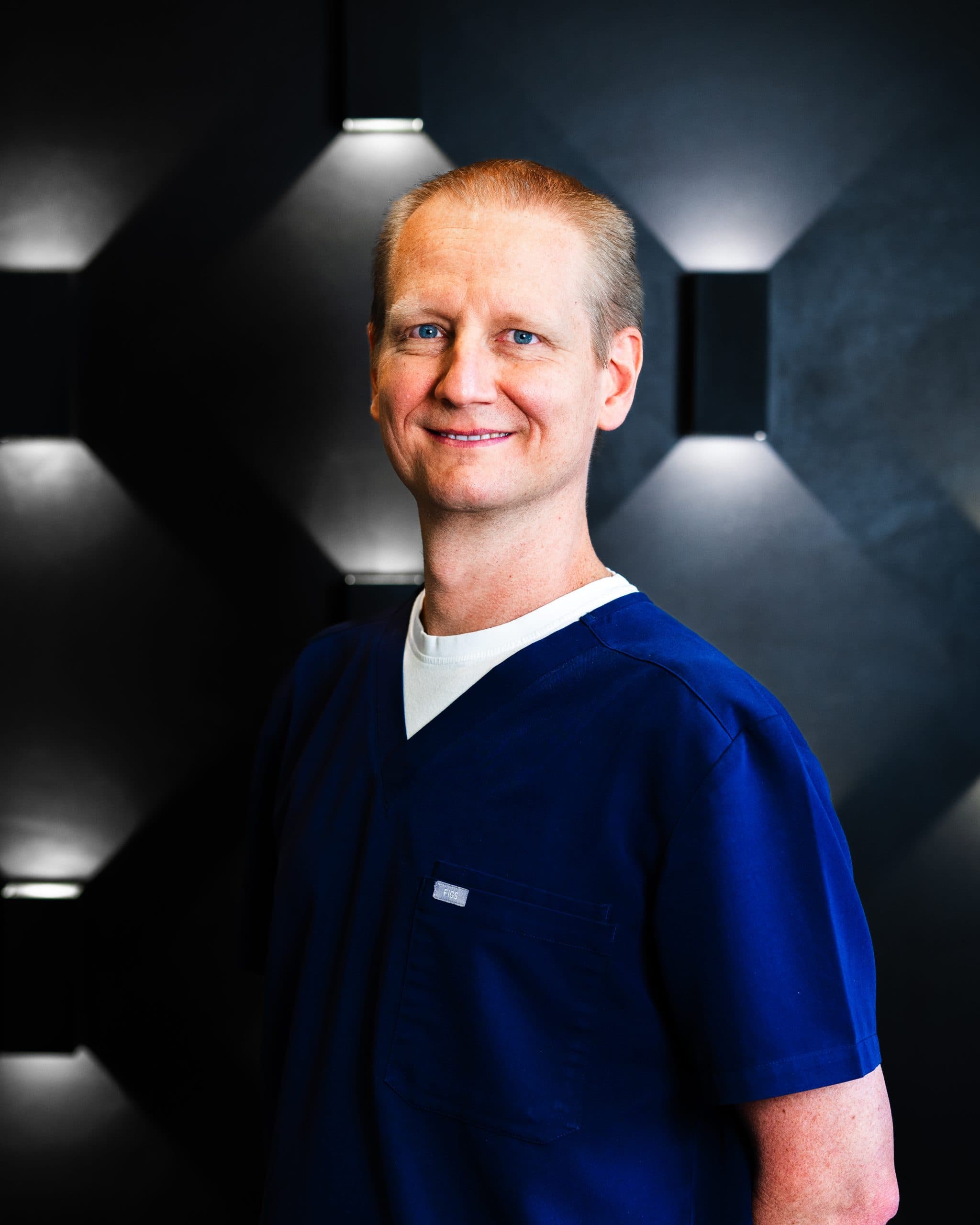 Dentist Dr Colin Bradshaw smiling wearing deep blue scrubs