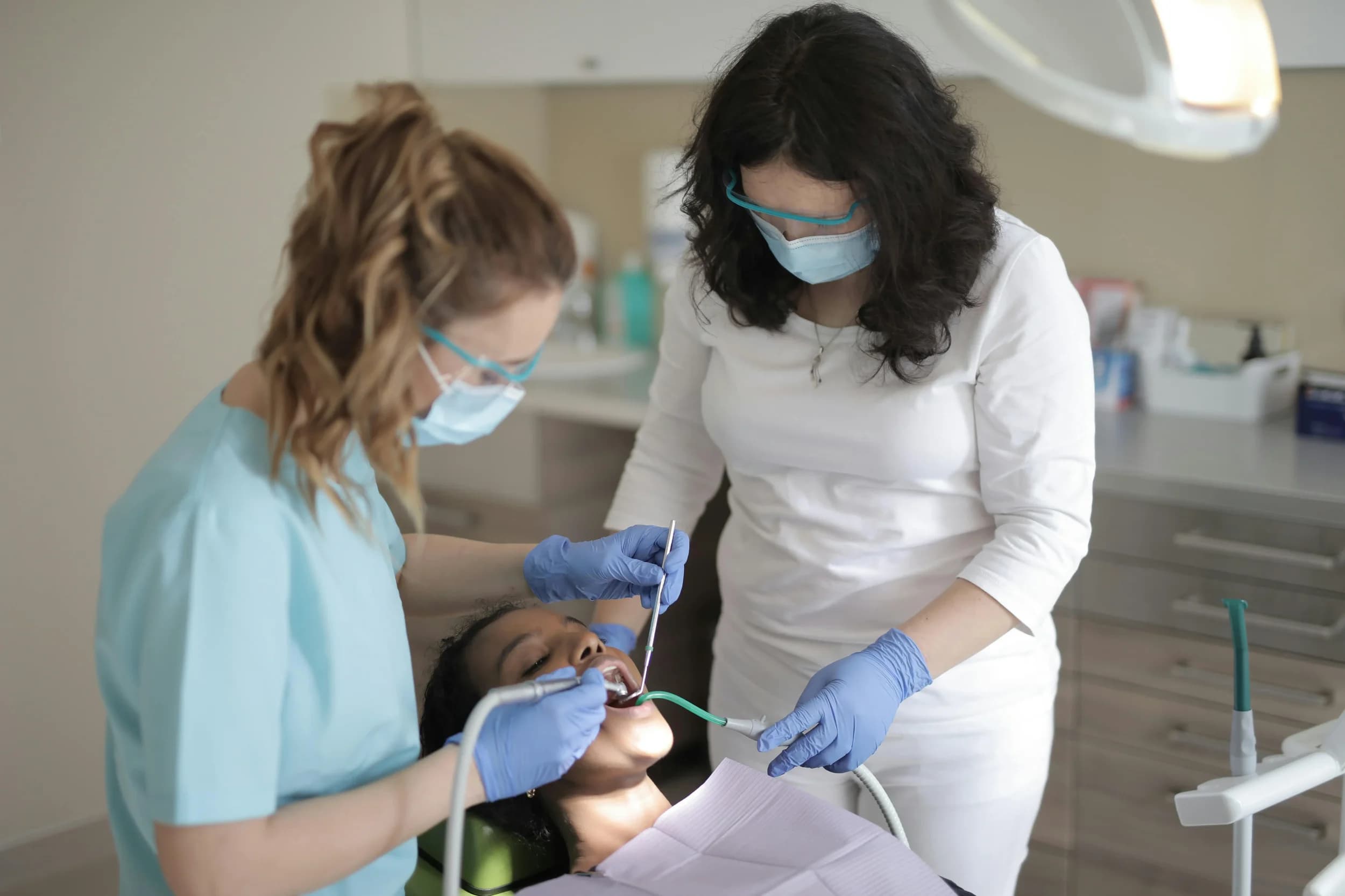 Young girl receiving dental treatment from two female dental professionals in a dental office.