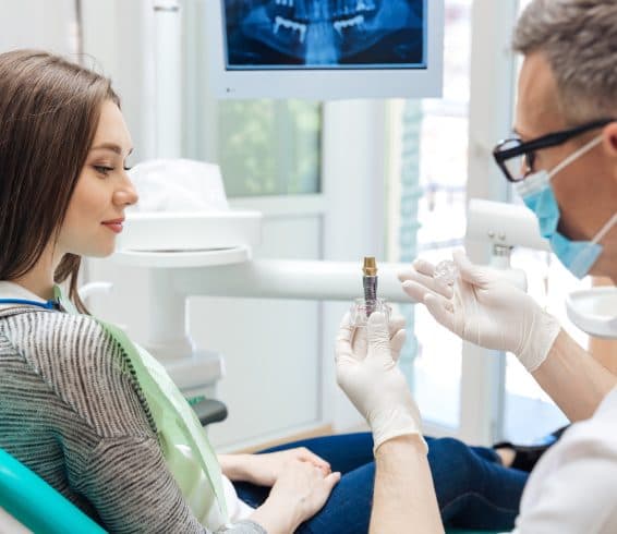 Male dentist showing his female patient a dental implant in clinic