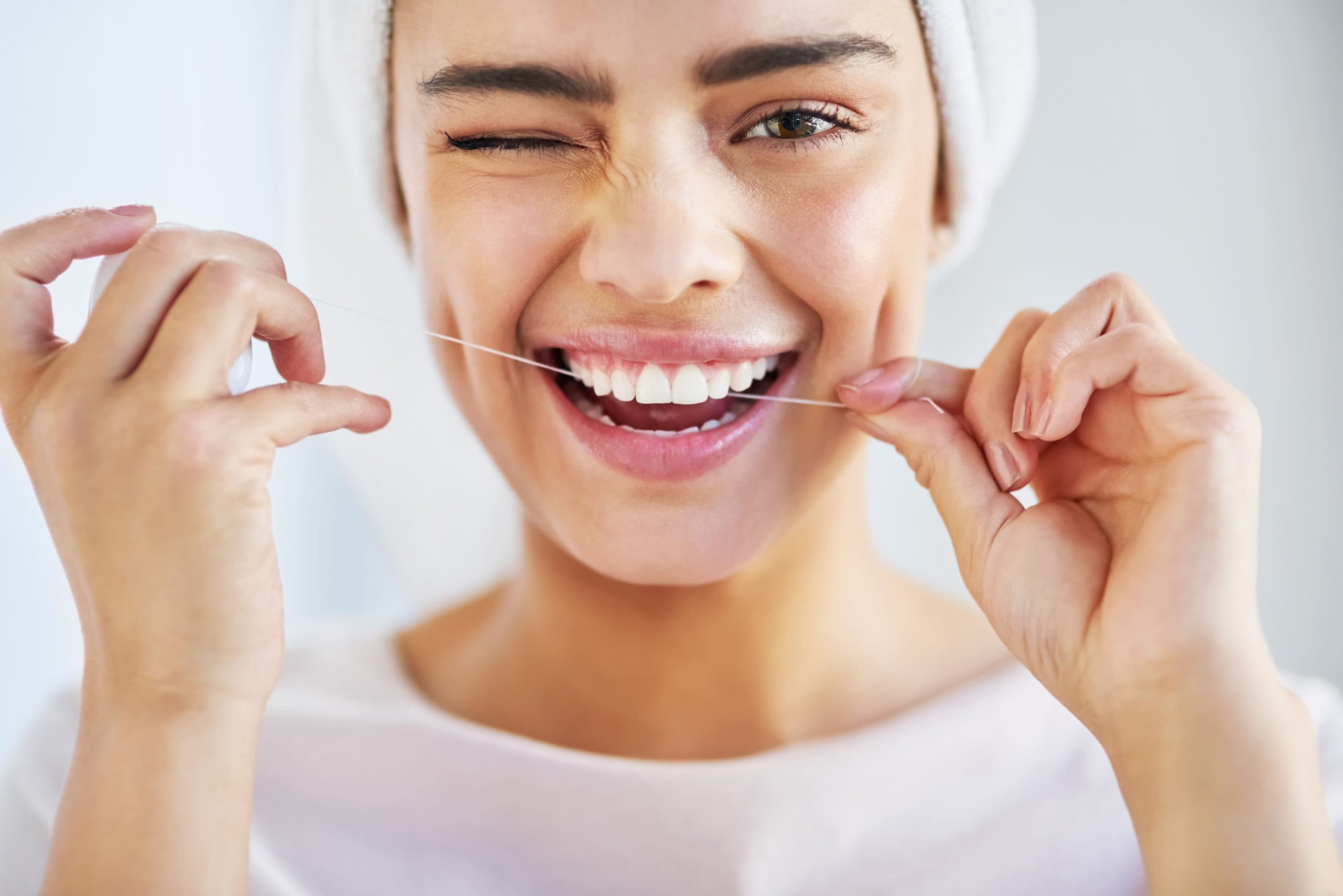 Smiling woman winking whilst flossing her teeth, illustrating the oral hygiene habits encouraged by a specialist orthodontist.