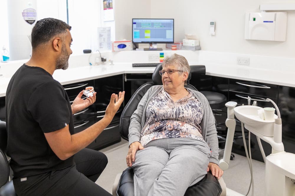Dentist explaining a dental model to a seated older woman in a modern dental clinic.