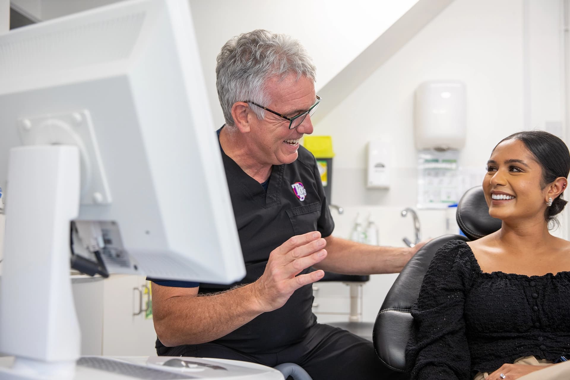 Smiling dentist talking to a female patient who is seated in a dental chair.